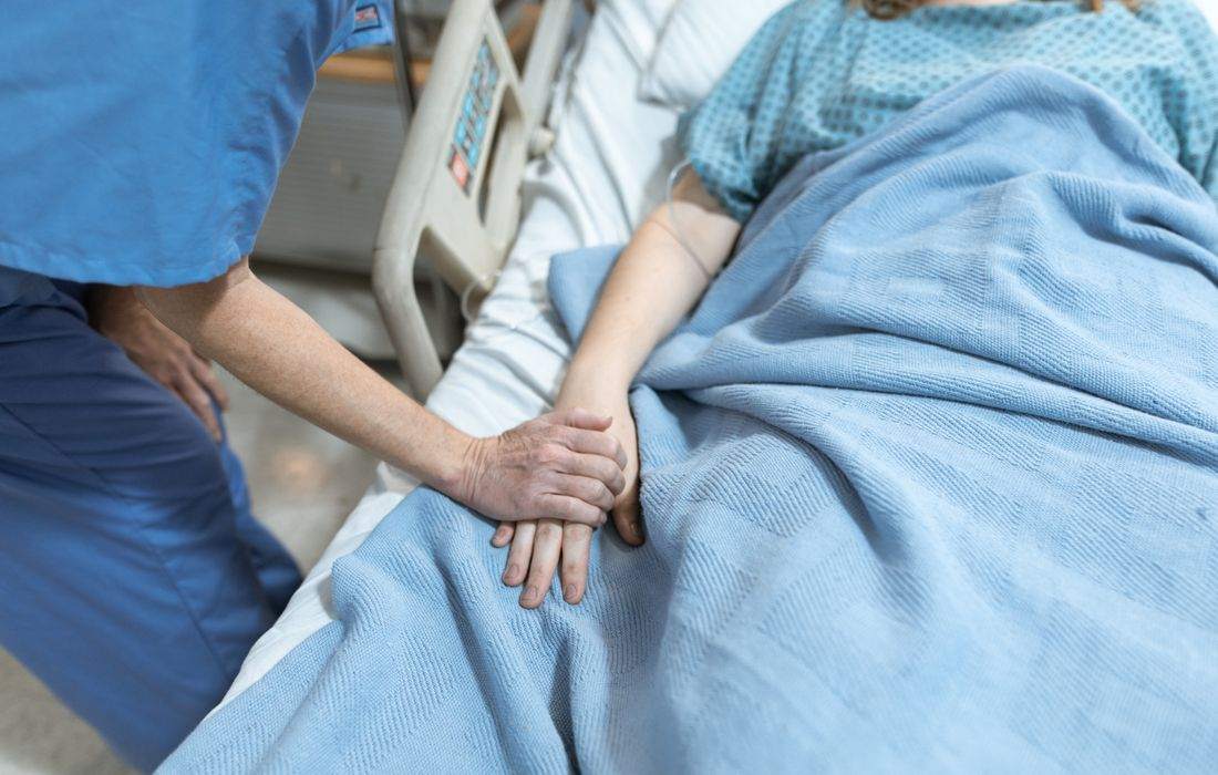 Profissional de saúde segurando a mão de uma paciente internada